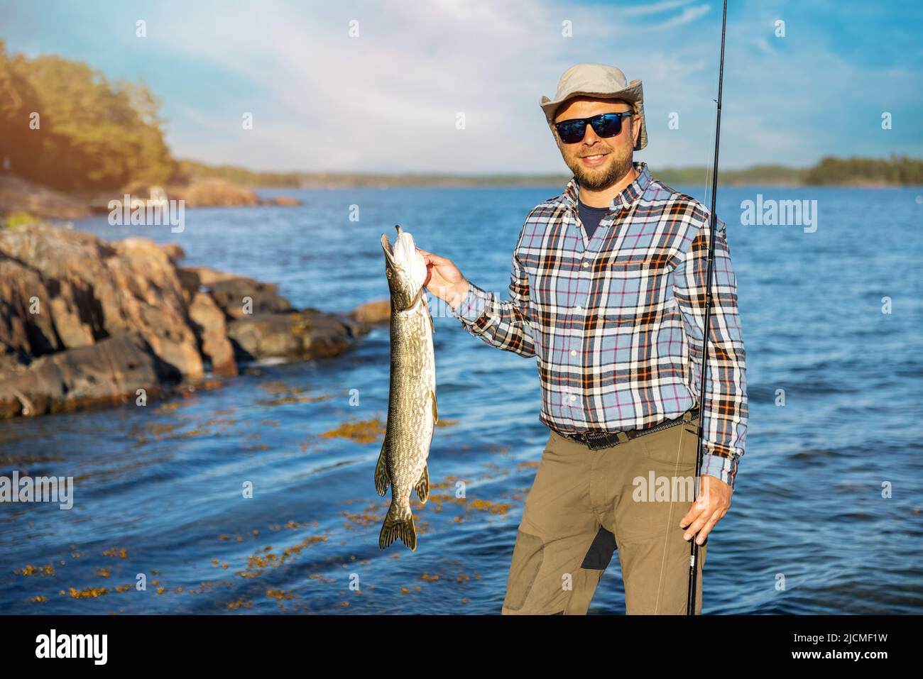pescador sonriente con peces de lucio capturados en la mano Foto de stock