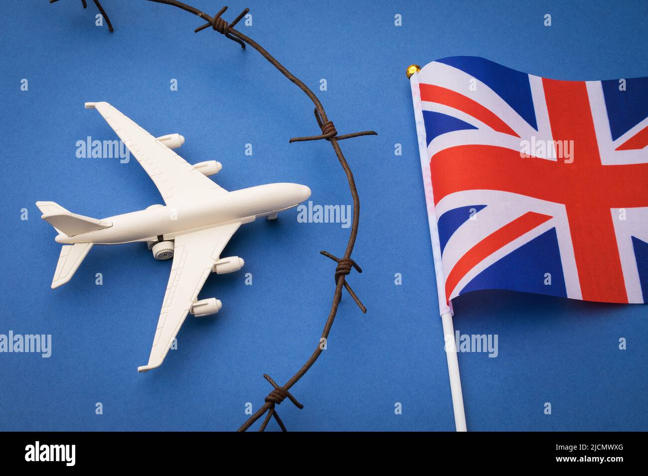 Avión de juguete, bandera y alambre de púas oxidadas sobre fondo de color, concepto de cierre de fronteras aéreas del Reino Unido Foto de stock