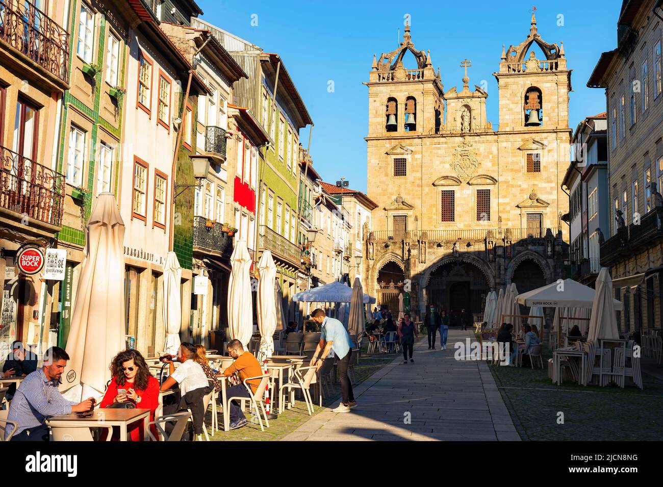 BRAGA, PORTUGAL - 14 DE NOVIEMBRE de 2021: Personas sentadas en el café de la calle, la iglesia de Santa Cruz en el fondo, el sol de la tarde Foto de stock