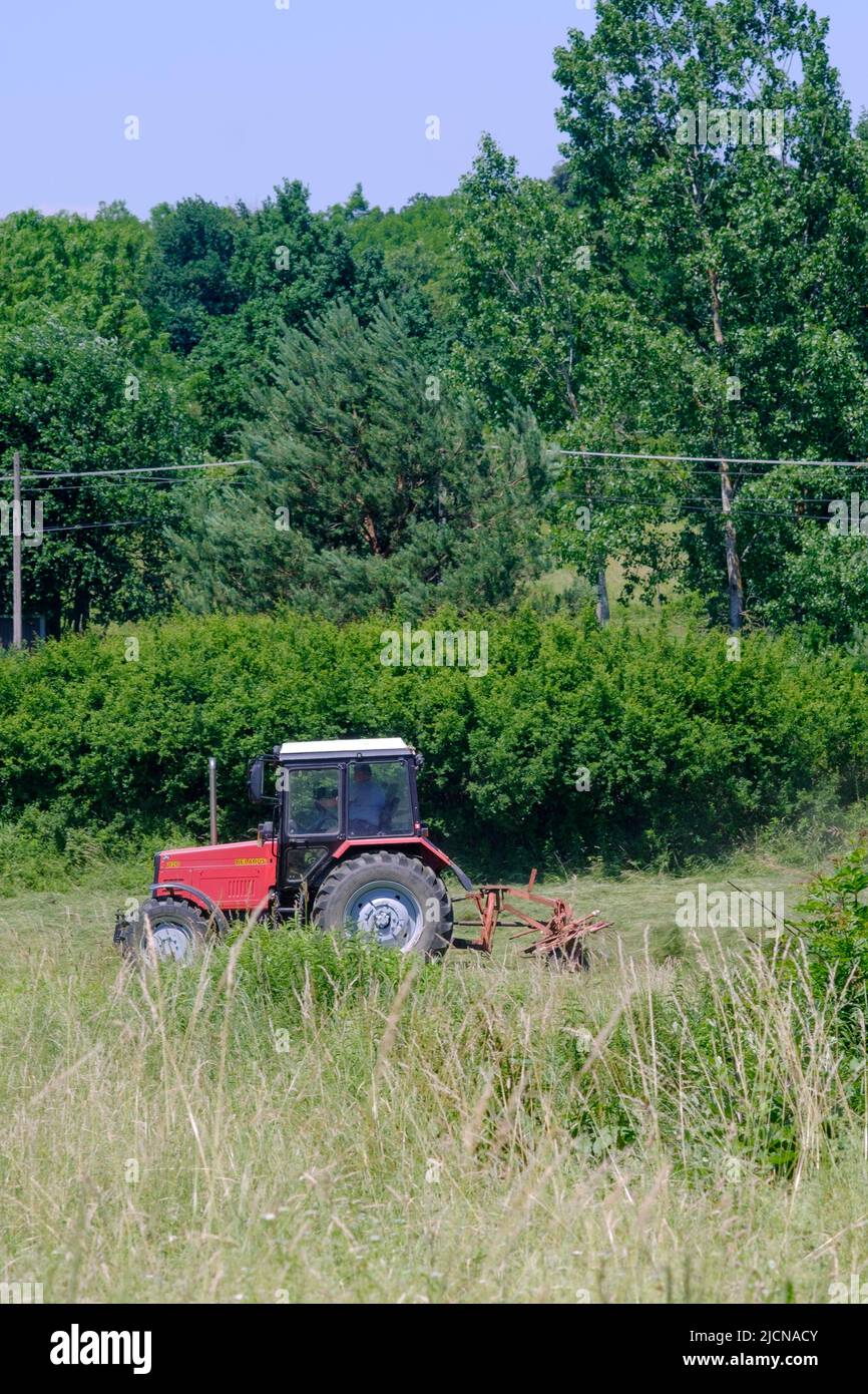 Agricultor usando un tractor rojo para trabajo en campo verde en una zona rural de la campiña del condado de Zala hungría Foto de stock