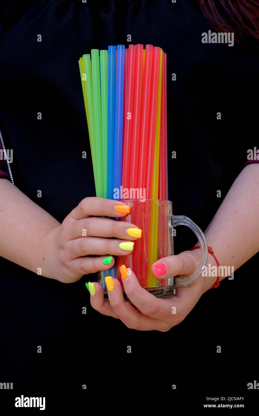 mujer con extensiones de uñas pintadas en una variedad de colores sosteniendo vidrio lleno de pajitas plásticas coloridas Foto de stock