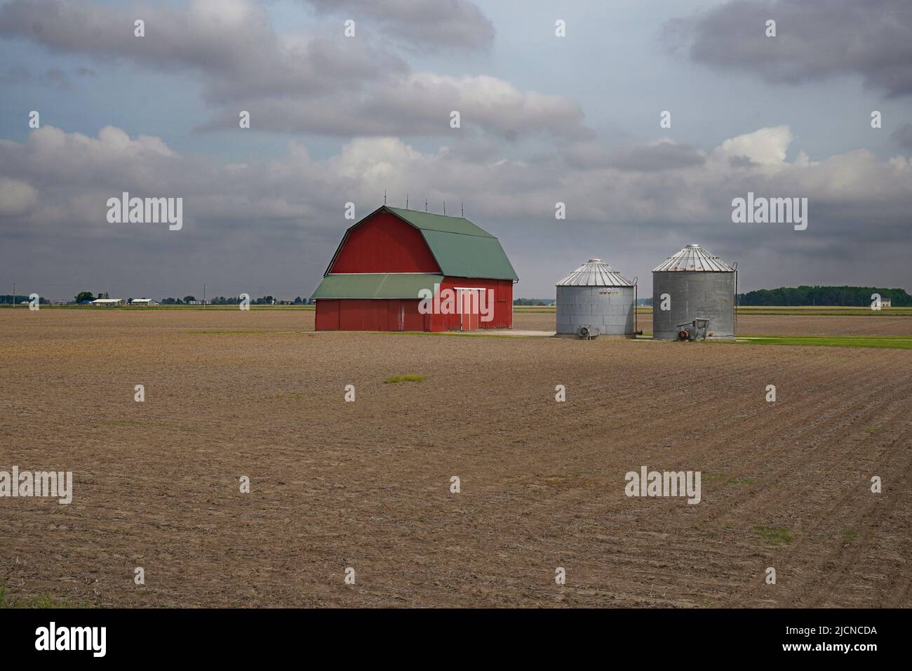 Escena agrícola con un granero rojo y dos silos rodeados por un campo recién arado en Ohio Foto de stock