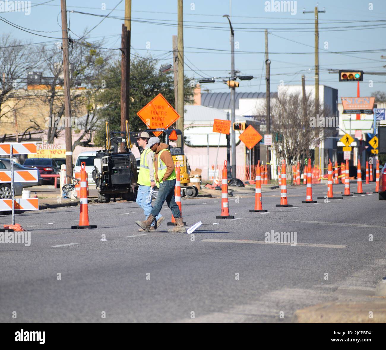 Trabajadores de la construcción de carreteras que caminan al otro lado de una calle en una zona de construcción Foto de stock