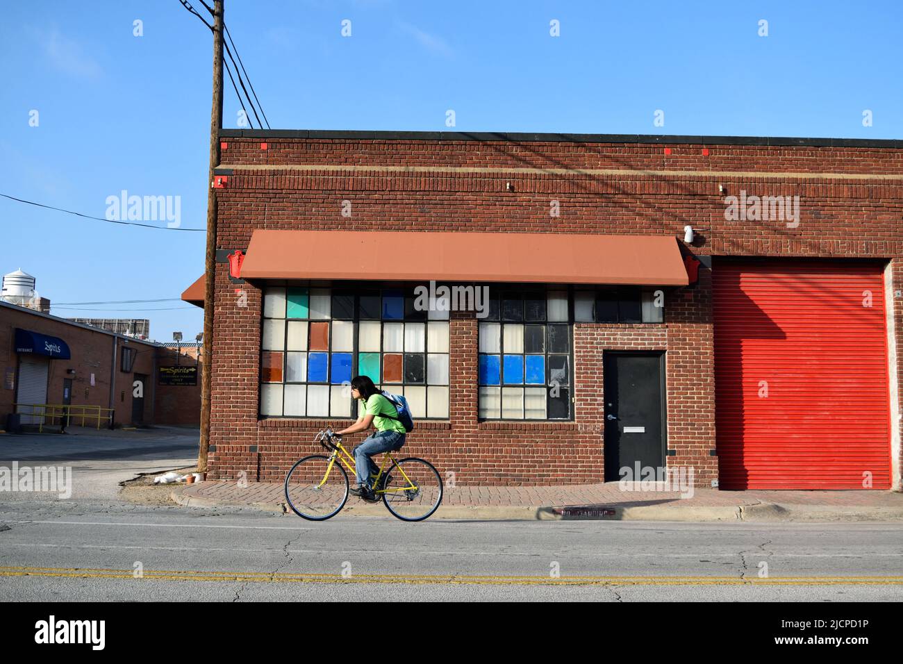 Montar en bicicleta frente a un antiguo edificio de ladrillo en la zona profunda de Elum de Dallas; coloridas ventanas en el edificio ca. 2014 Foto de stock