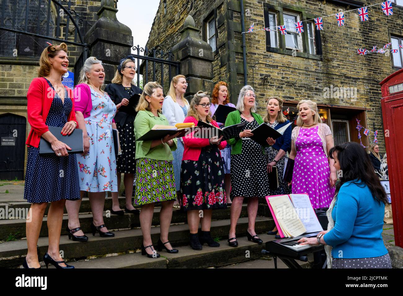 Haworth 1940 retro vivir historia evento (coro de mujeres tocando música, teclista, Unión Jack bunting) - Main Street, West Yorkshire Inglaterra Reino Unido Foto de stock