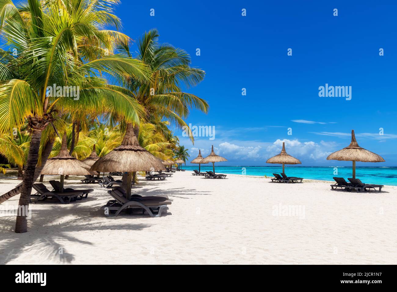 Hermosa playa con palmeras y sombrillas de paja en un complejo tropical en la isla Paradise. Foto de stock