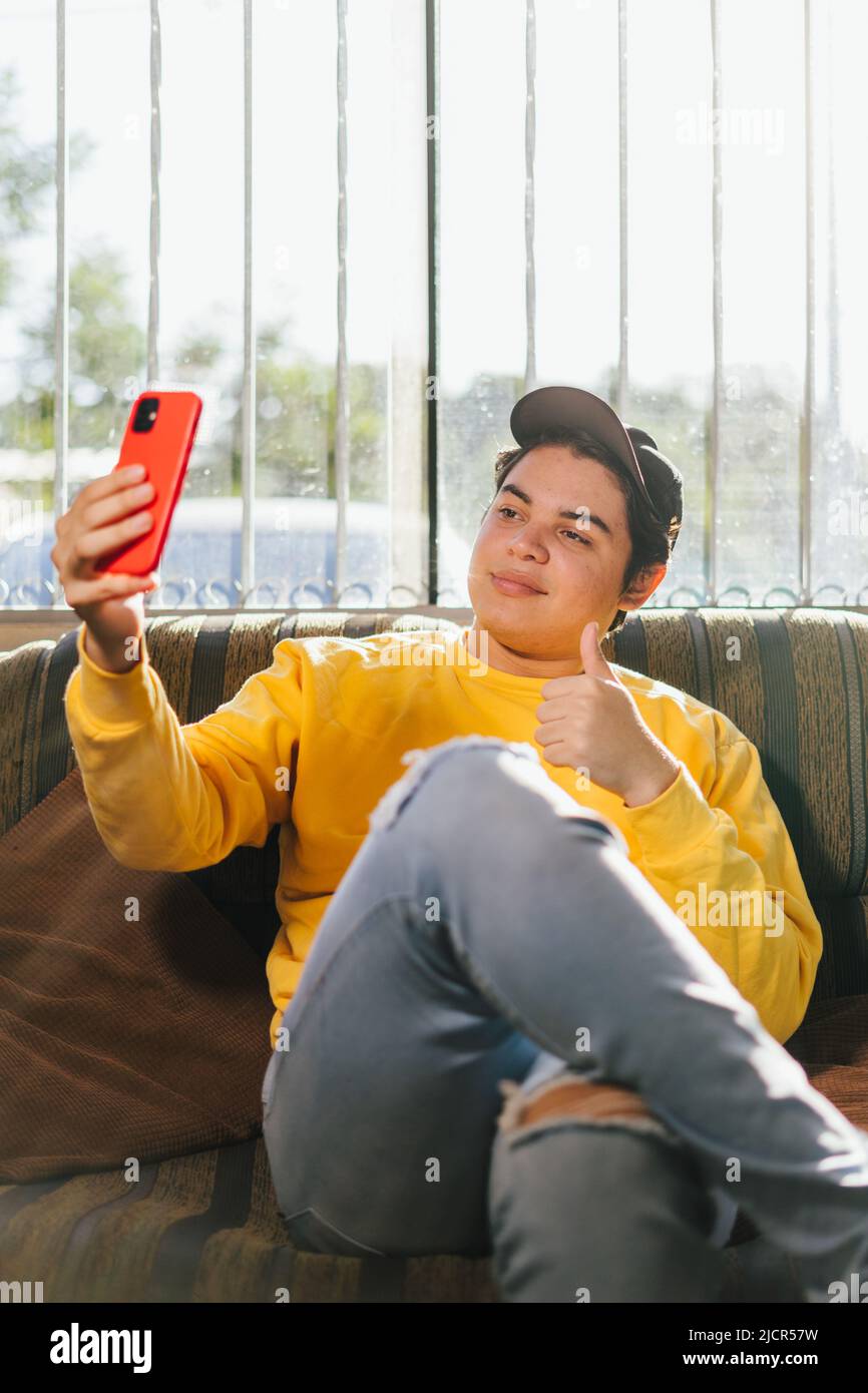 Amigable 20s joven con gorra negra, con camiseta de color amarillo tomando selfie en el poste del teléfono celular. Foto en la red social que agita la mano es Foto de stock