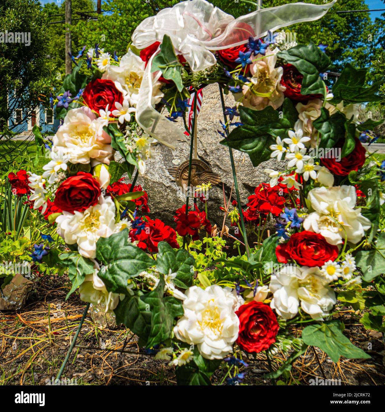 Corona del Día de los Caídos de flores rojas, blancas y azules para conmemorar a los veteranos de guerra en un verde de pueblo de Nueva Inglaterra Foto de stock
