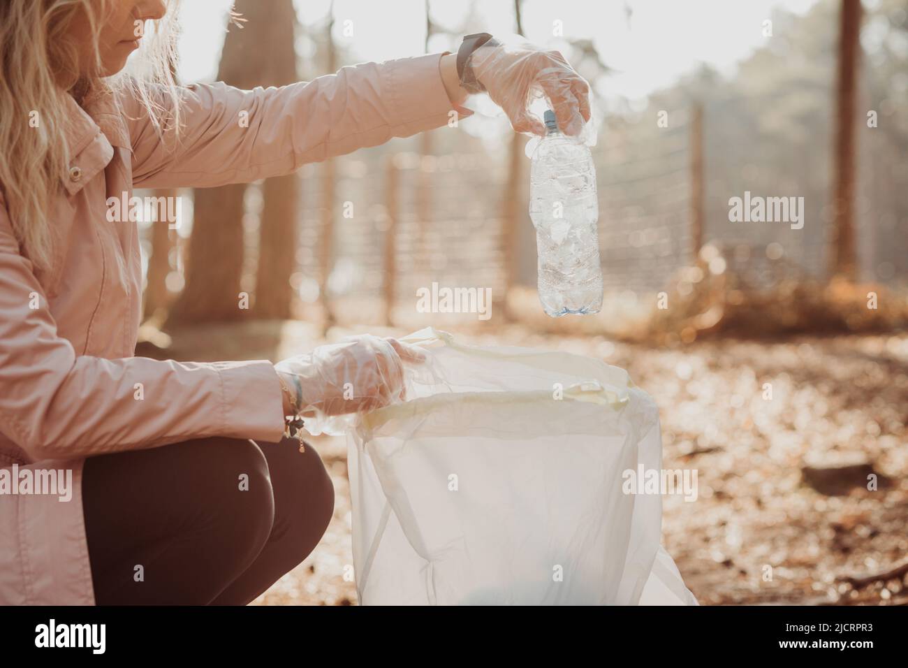 La activista de la mujer recortada ayuda a limpiar el bosque de los desechos plásticos, la basura. Recoja la botella en la bolsa. Reciclaje ecológico mundial Foto de stock