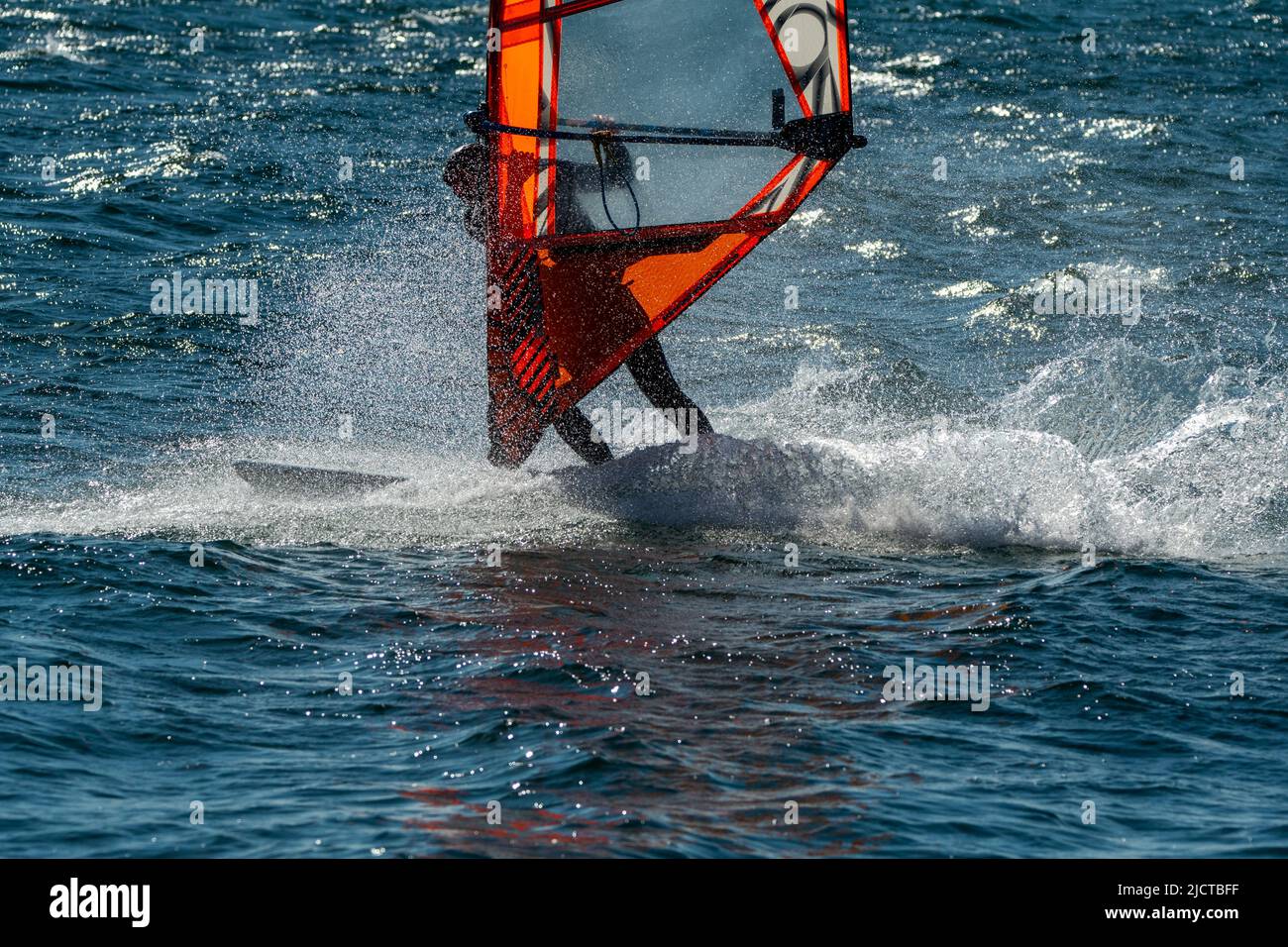 Windsurfer está practicando en este hermoso y ventoso día de primavera. Está aprendiendo a cambiar de dirección a través de un movimiento de giro acrobático. Foto de stock