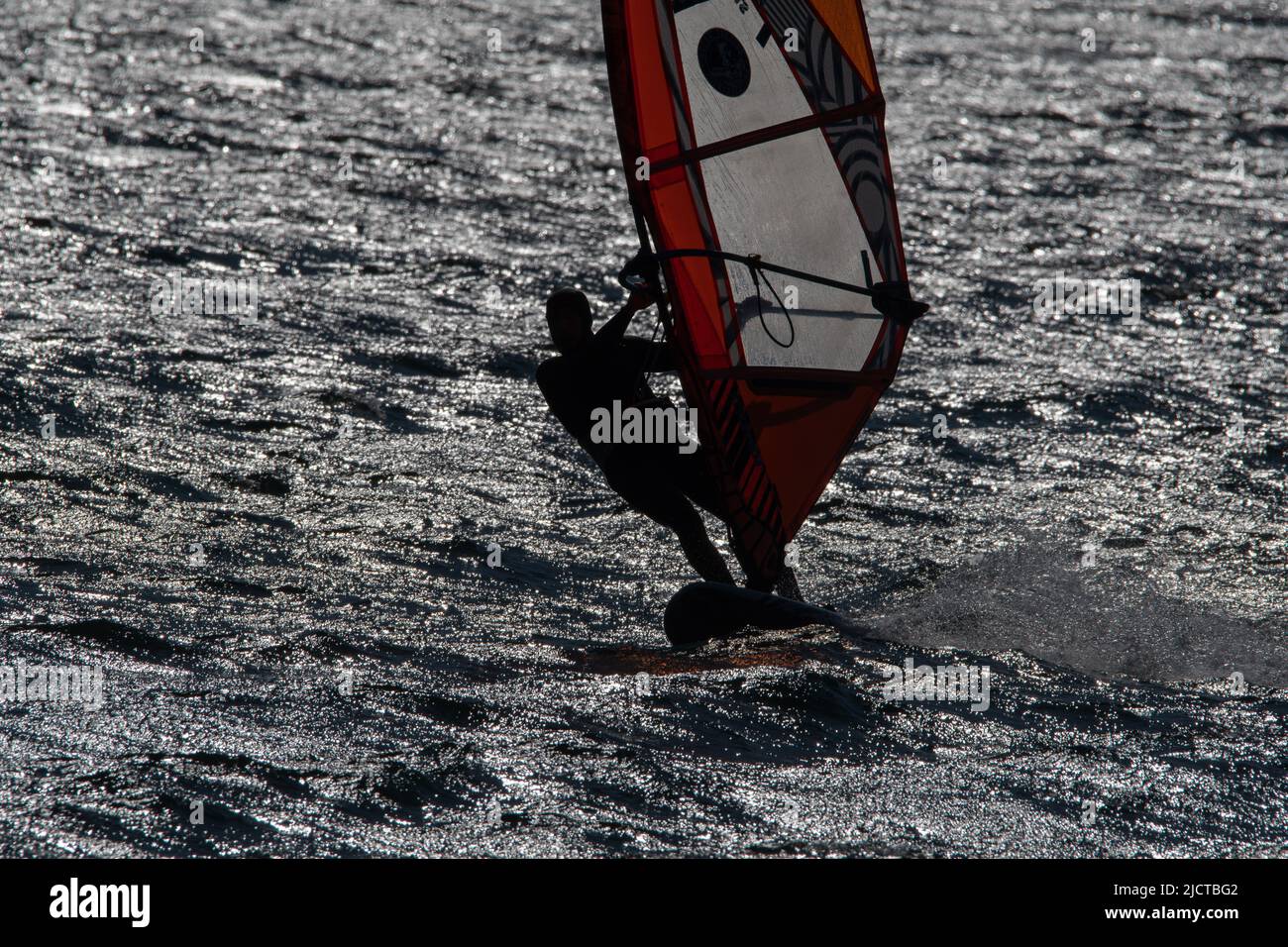 Windsurfer está practicando en este hermoso y ventoso día de primavera. Está aprendiendo a cambiar de dirección a través de un movimiento de giro acrobático. Foto de stock