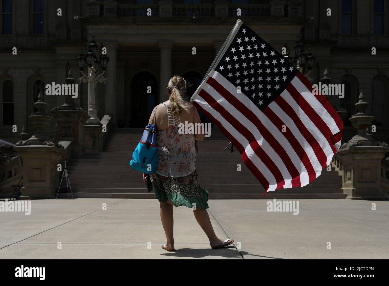 Una mujer está en frente del Capitolio del Estado de Michigan con una bandera estadounidense durante un evento de Marcha por la Libertad Médica organizado por Informed Choice Michigan en Lansing, Michigan, EE.UU., 15 de junio de 2022. REUTERS/Emily Elconin Foto de stock