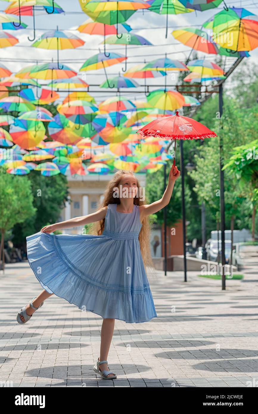 Una chica muy pequeña saltando mientras sostiene un paraguas rojo. Hermoso niño volando Foto de stock