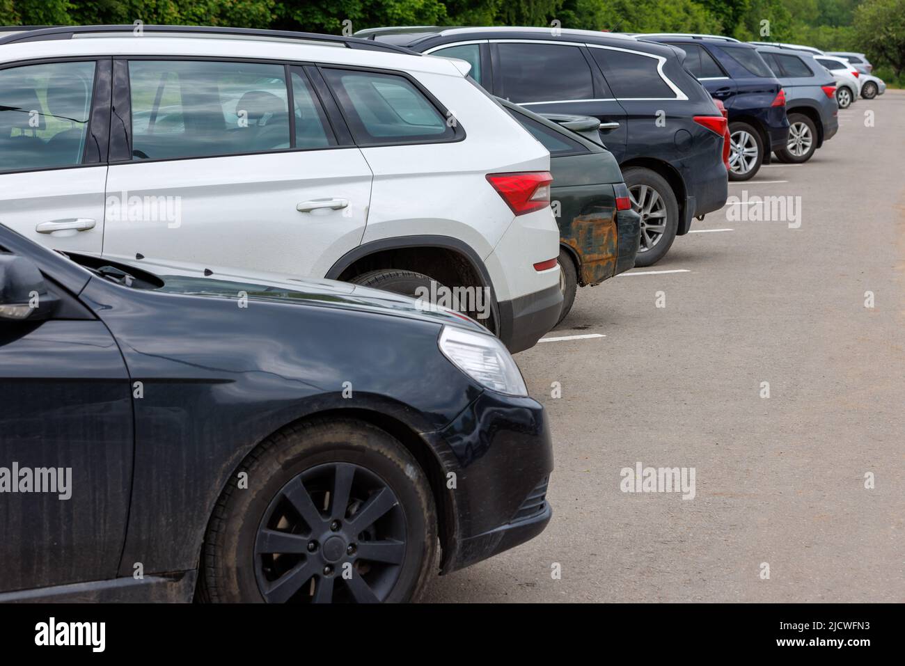 fila de coches de diferentes colores en el estacionamiento de asfalto en el día nublado del verano Foto de stock