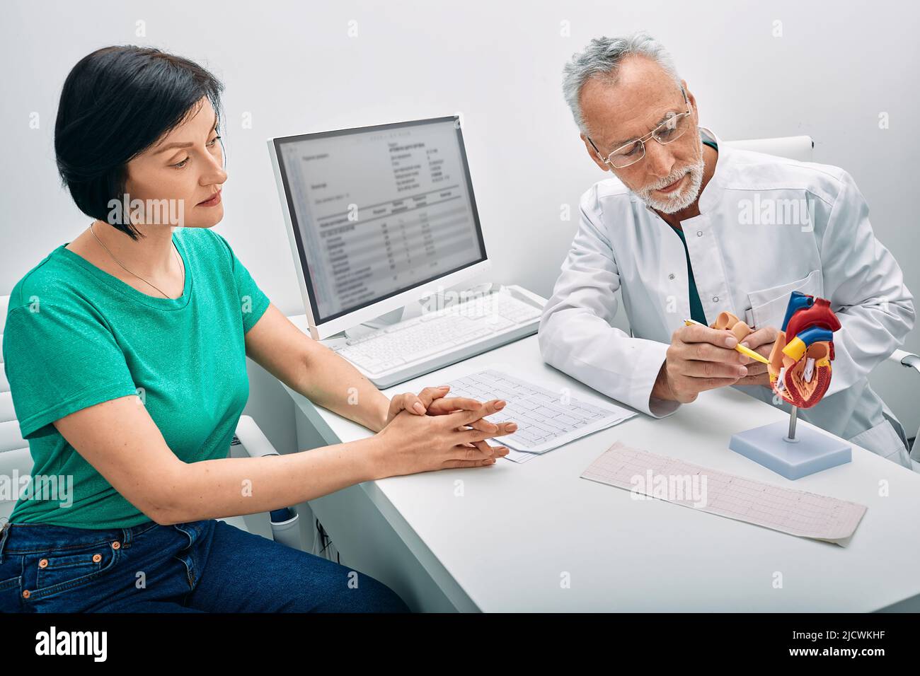 Cardiólogo que muestra la estructura y anatomía del corazón humano utilizando el modelo de enseñanza médica del corazón mientras consulta a la paciente femenina Foto de stock