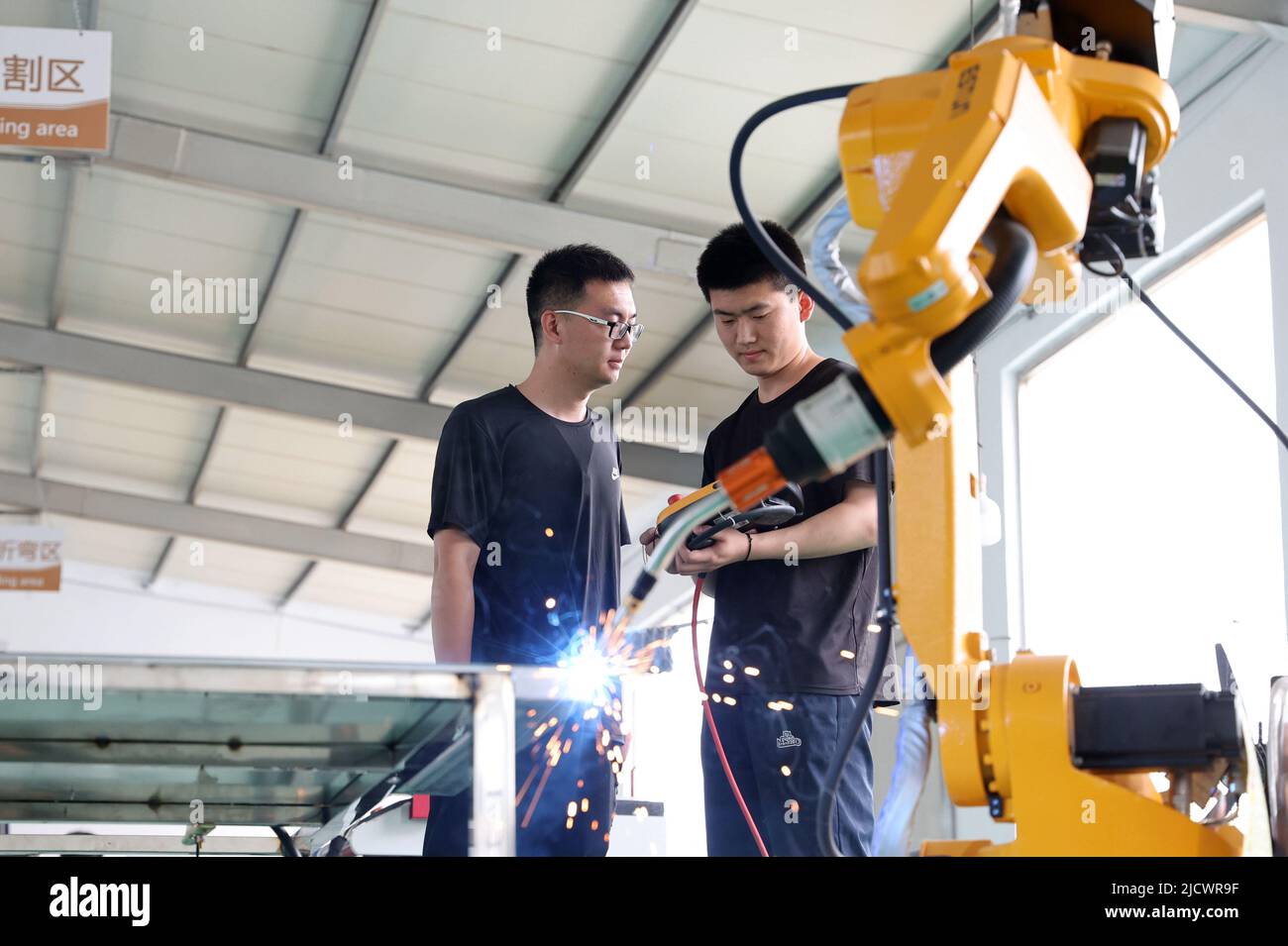 BINZHOU, CHINA - 16 DE JUNIO de 2022 - Dos técnicos depuran un producto de pedido de un robot industrial recientemente desarrollado en la tecnología electrónica de punto negro Foto de stock