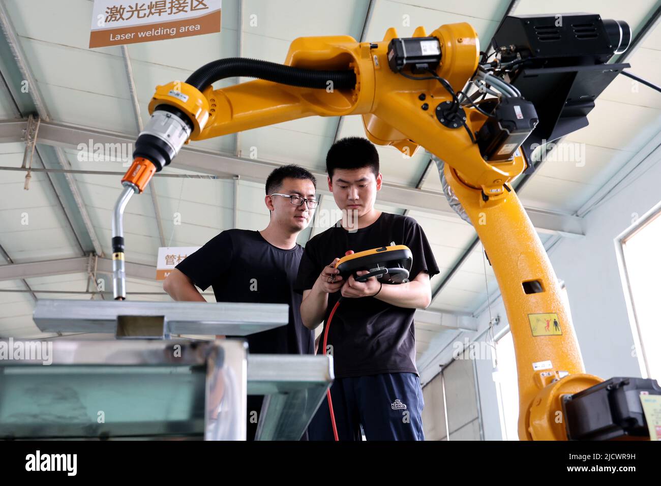 BINZHOU, CHINA - 16 DE JUNIO de 2022 - Dos técnicos depuran un producto de pedido de un robot industrial recientemente desarrollado en la tecnología electrónica de punto negro Foto de stock