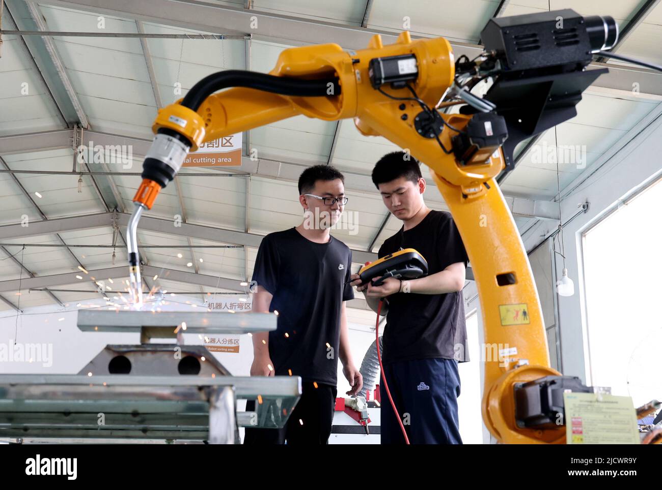 BINZHOU, CHINA - 16 DE JUNIO de 2022 - Dos técnicos depuran un producto de pedido de un robot industrial recientemente desarrollado en la tecnología electrónica de punto negro Foto de stock