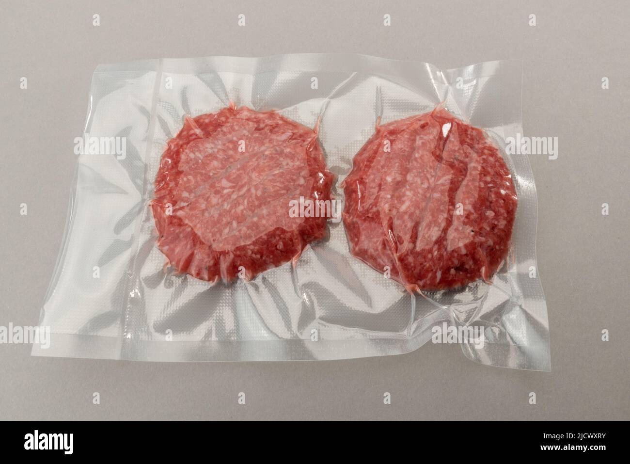 Hamburguesa de carne para hamburguesa en envasado al vacío sellado para cocinar al vacío aislado sobre fondo gris Foto de stock