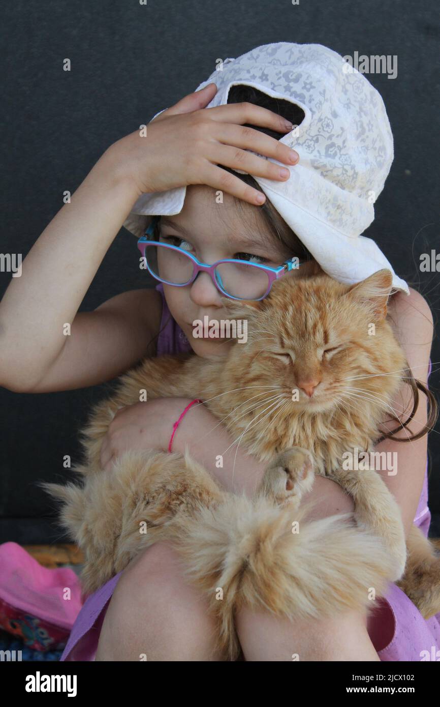 niña pequeña jugar en el jardín de verano con su gato rojo esponjoso Foto de stock