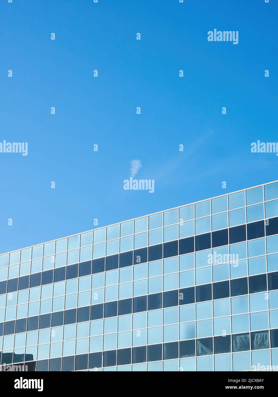 Una meditación abstracta sobre la vida de oficina - un cielo azul iluminado por el sol aparentemente enjaulado por las ventanas del edificio que lo reflejan, con una nube sobre el cielo abierto. Foto de stock