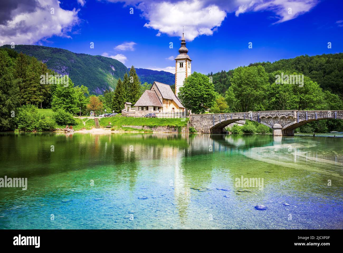 Lago Bohinj, Eslovenia. Iglesia de San Juan Bautista con puente sobre el río Sava. Parque Nacional Triglav en los Alpes Julianos. Foto de stock