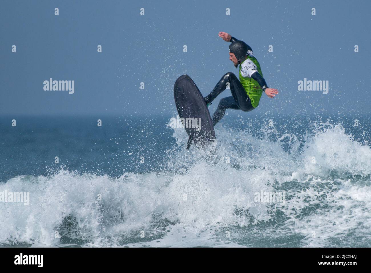 Un surfista masculino que lleva un casco de seguridad compitiendo en una competición de surf en Fistral en Newquay en Cornwall en el Reino Unido. Foto de stock