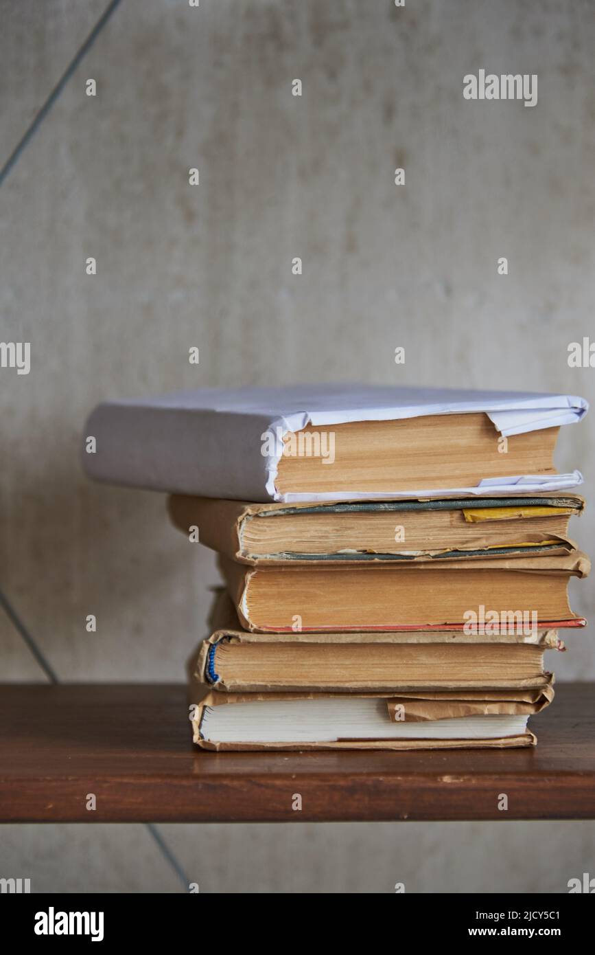 Una pila de libros viejos en un estante contra una pared gris. Foto de stock
