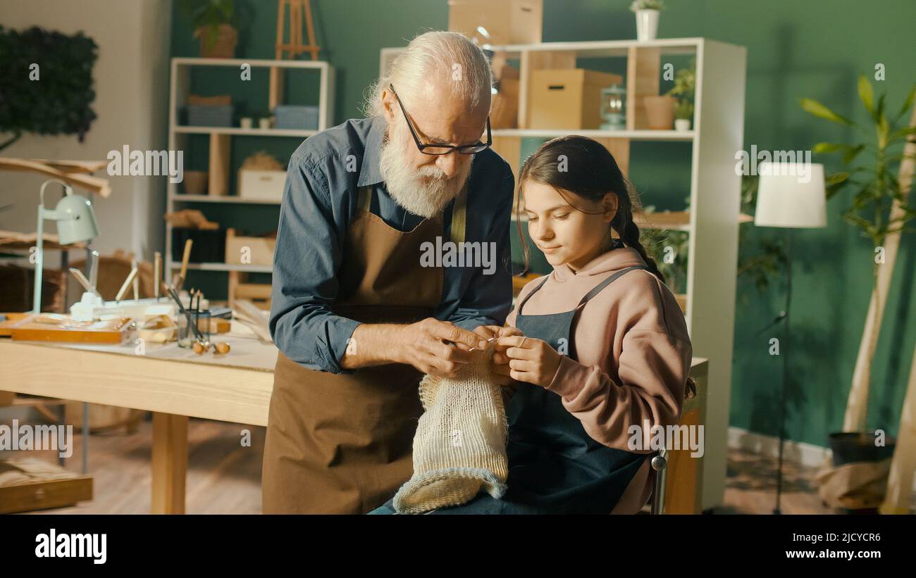 Un abuelo de Caring enseña a su nieta adolescente a coser en el taller Foto de stock