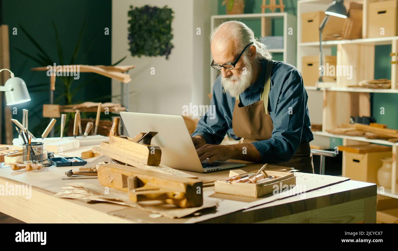 Un carpintero centrado desarrolla diseños a partir de bocetos de los modelos de madera 3D utilizando un ordenador portátil Foto de stock