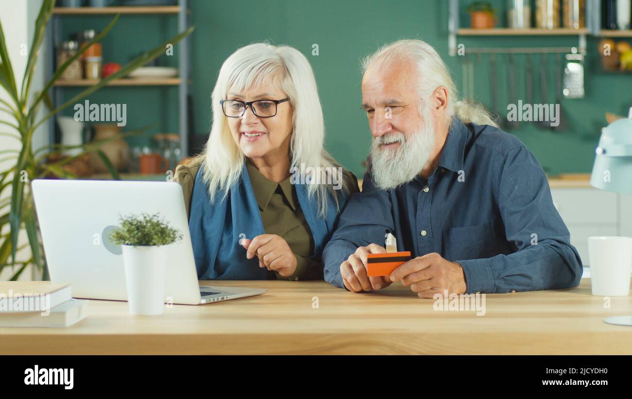 Feliz pareja de ancianos Compra en línea desde casa usando computadora y tarjeta de crédito. Foto de stock