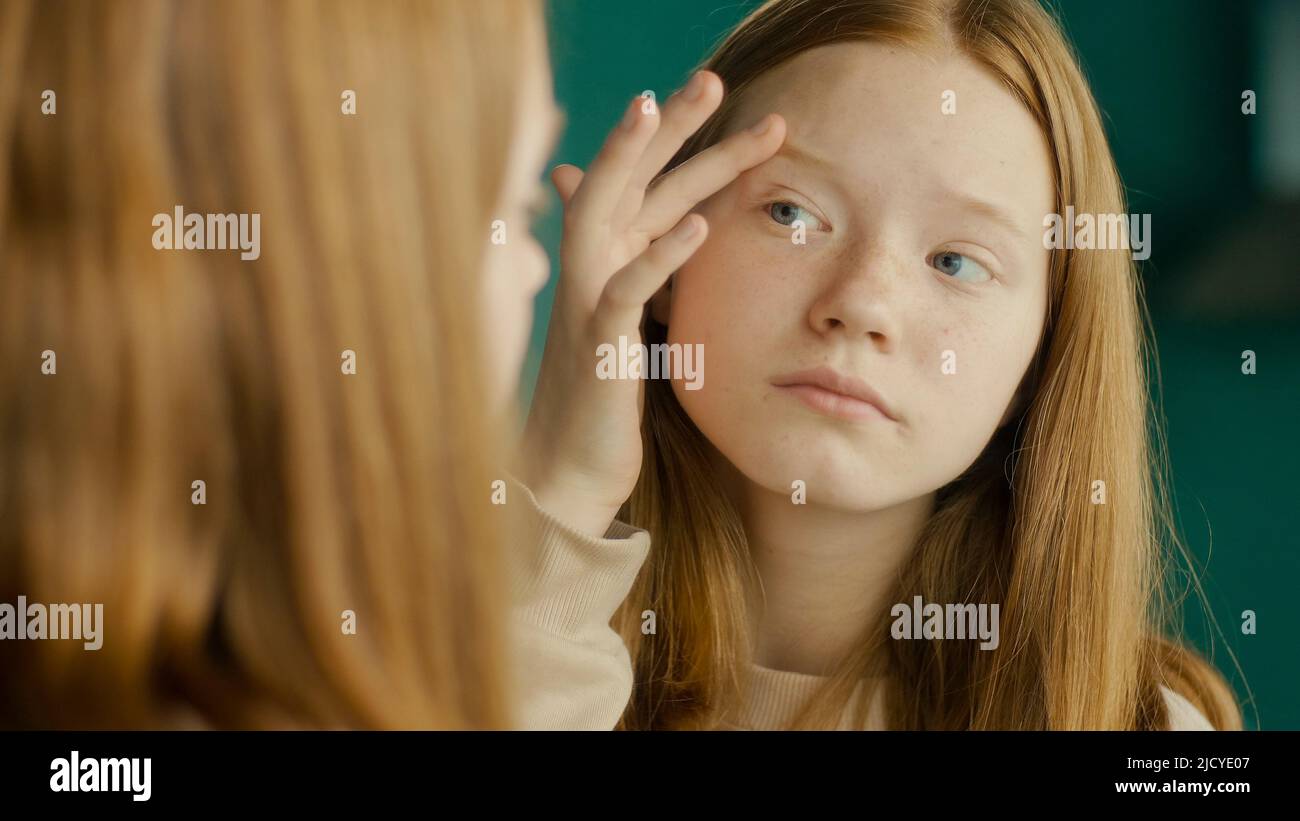 Una niña adolescente de pelo rojo examina su reflejo en el espejo. Adolescencia Foto de stock