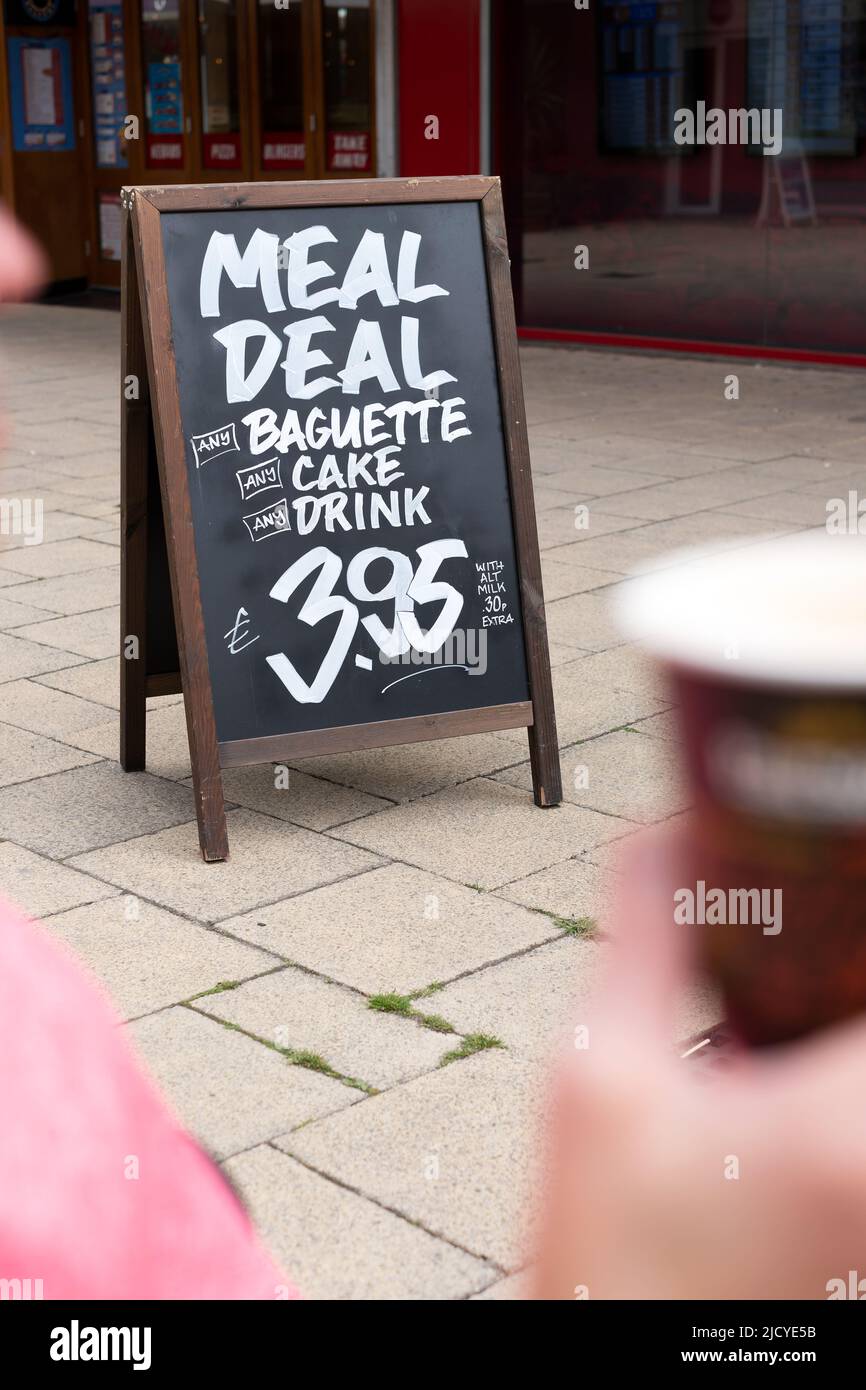 Un cartel de sandboard en un distrito comercial del reino unido que anuncia una oferta de comida barata en una panadería cercana. La oferta ofrece una bebida, pastel y baguette Foto de stock