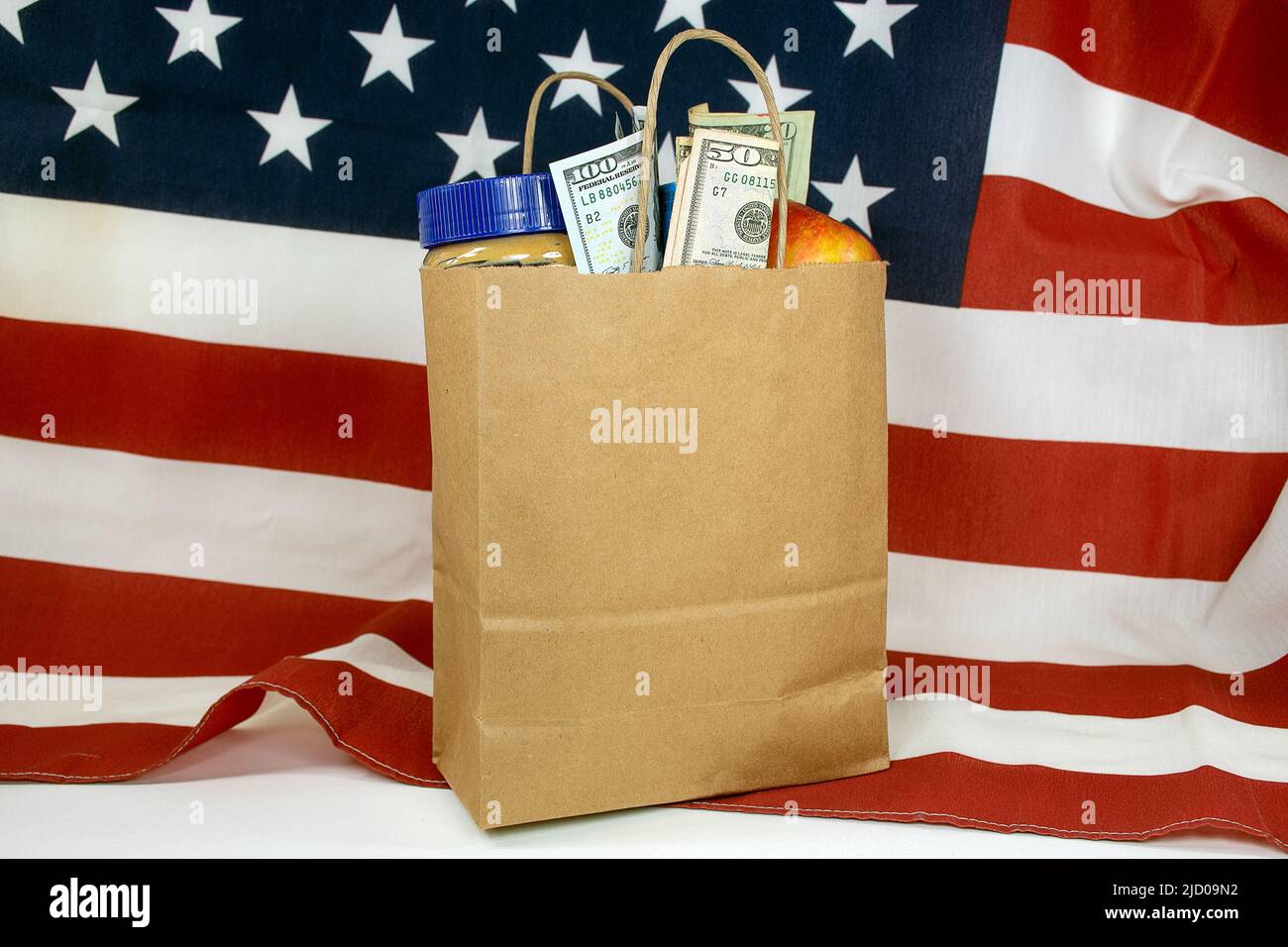 Una bolsa de papel marrón normal llena de comestibles y dinero en una bandera americana Foto de stock