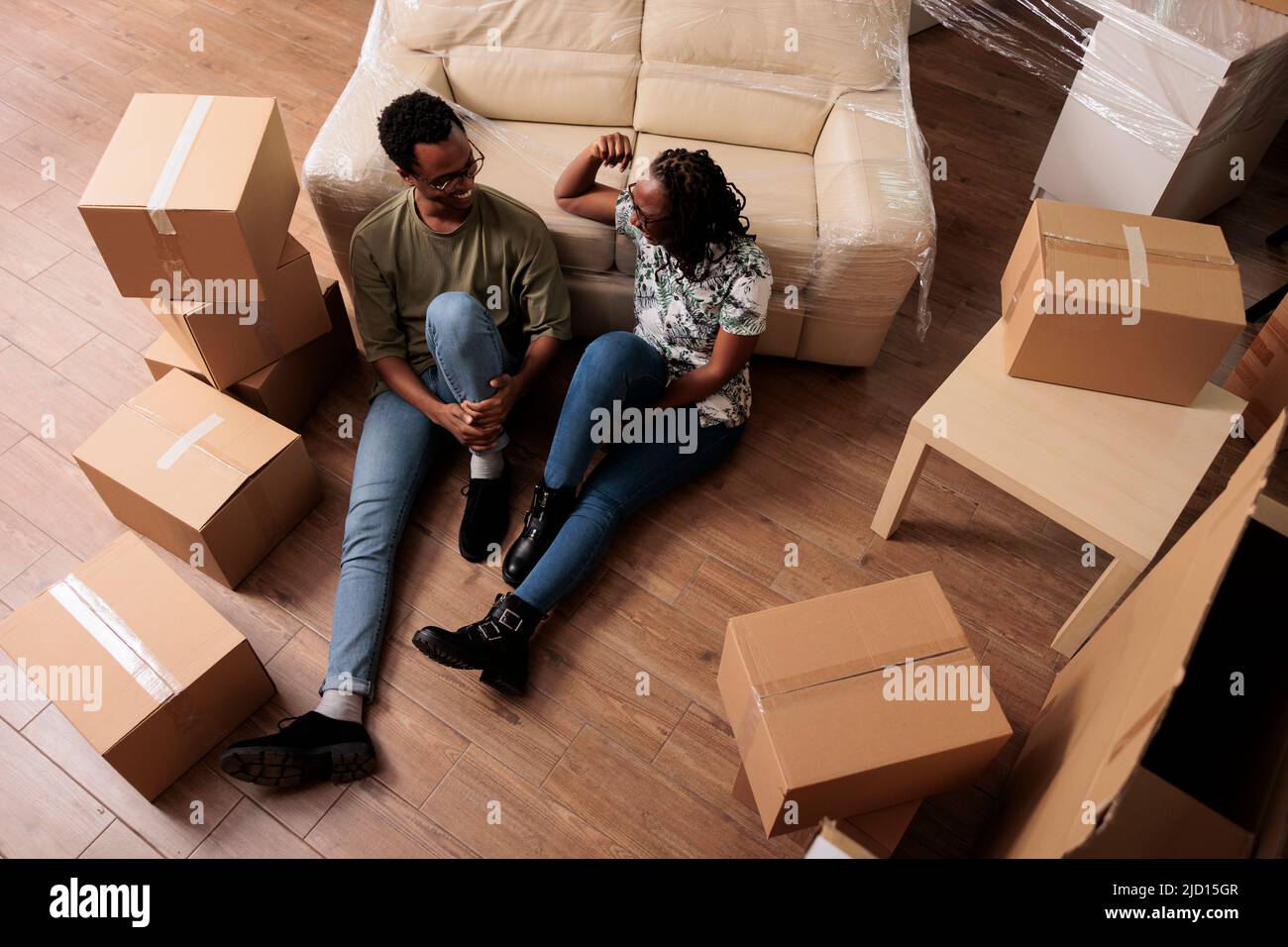 Pareja afroamericana disfrutando de una nueva propiedad familiar, tomando un descanso en el piso después de mudarse juntos. Relajarse en el día de la mudanza, comprando la primera casa de apartamento en préstamo hipotecario. Vista superior de. Foto de stock