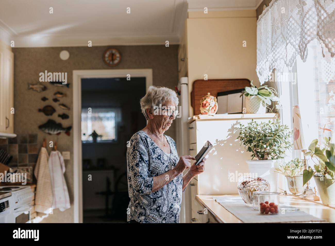 Mujer mayor usando el teléfono celular en la cocina Foto de stock