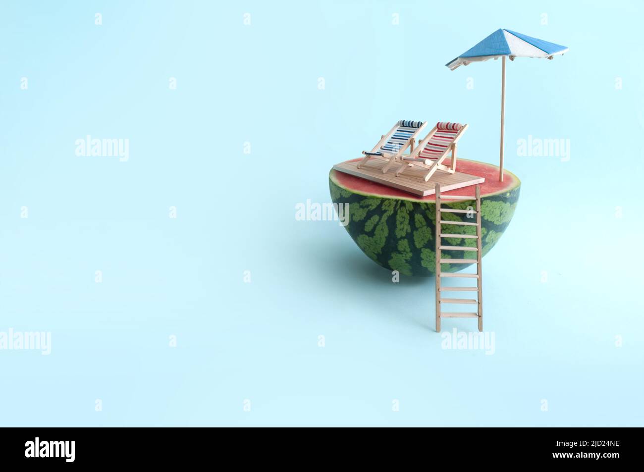 Concepto de vacaciones de verano en la playa, sandía con sombrilla, dos tumbonas y escalera de madera en la playa Foto de stock