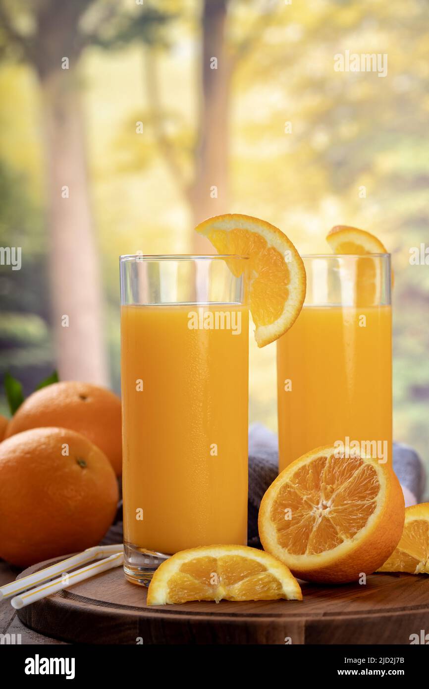 Dos vasos de zumo de naranja con rodajas de naranja sobre un fondo rural de verano Foto de stock