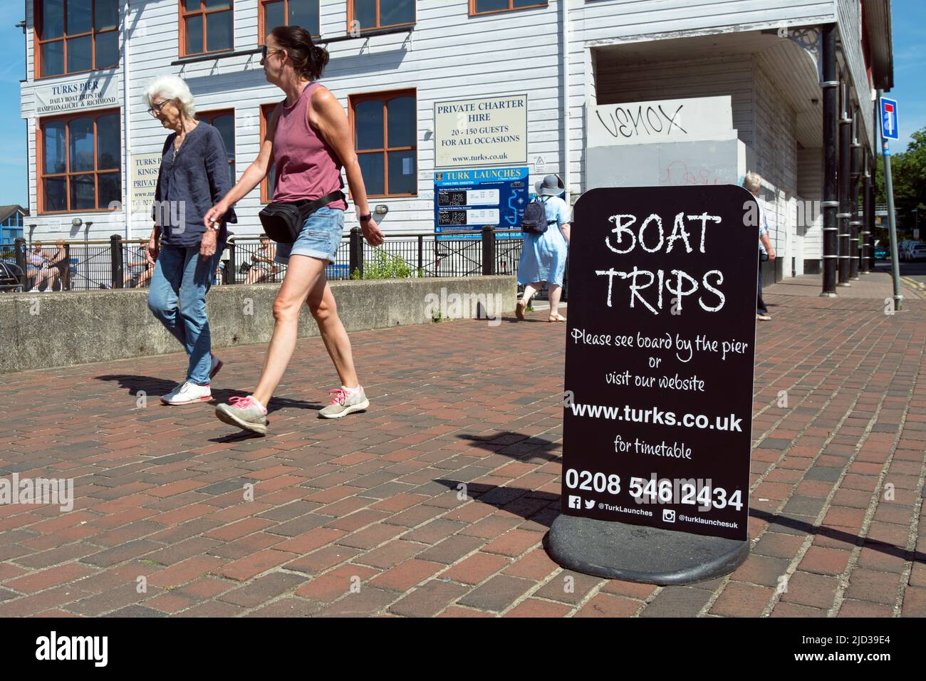dos mujeres caminan por un cartel para viajes en barco, dirigido por una compañía llamada turks, en kingston upon thames, surrey, inglaterra Foto de stock
