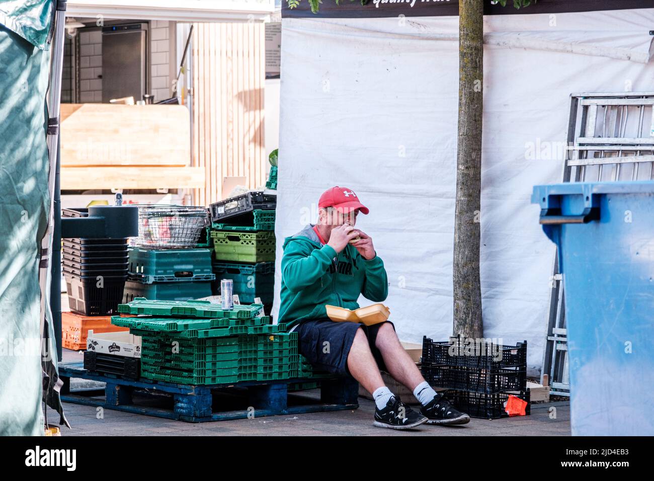 Epsom Surrey, Londres, 11 2022 de junio, Hombre sentado solo comiendo hamburguesa con gorra roja de béisbol Foto de stock