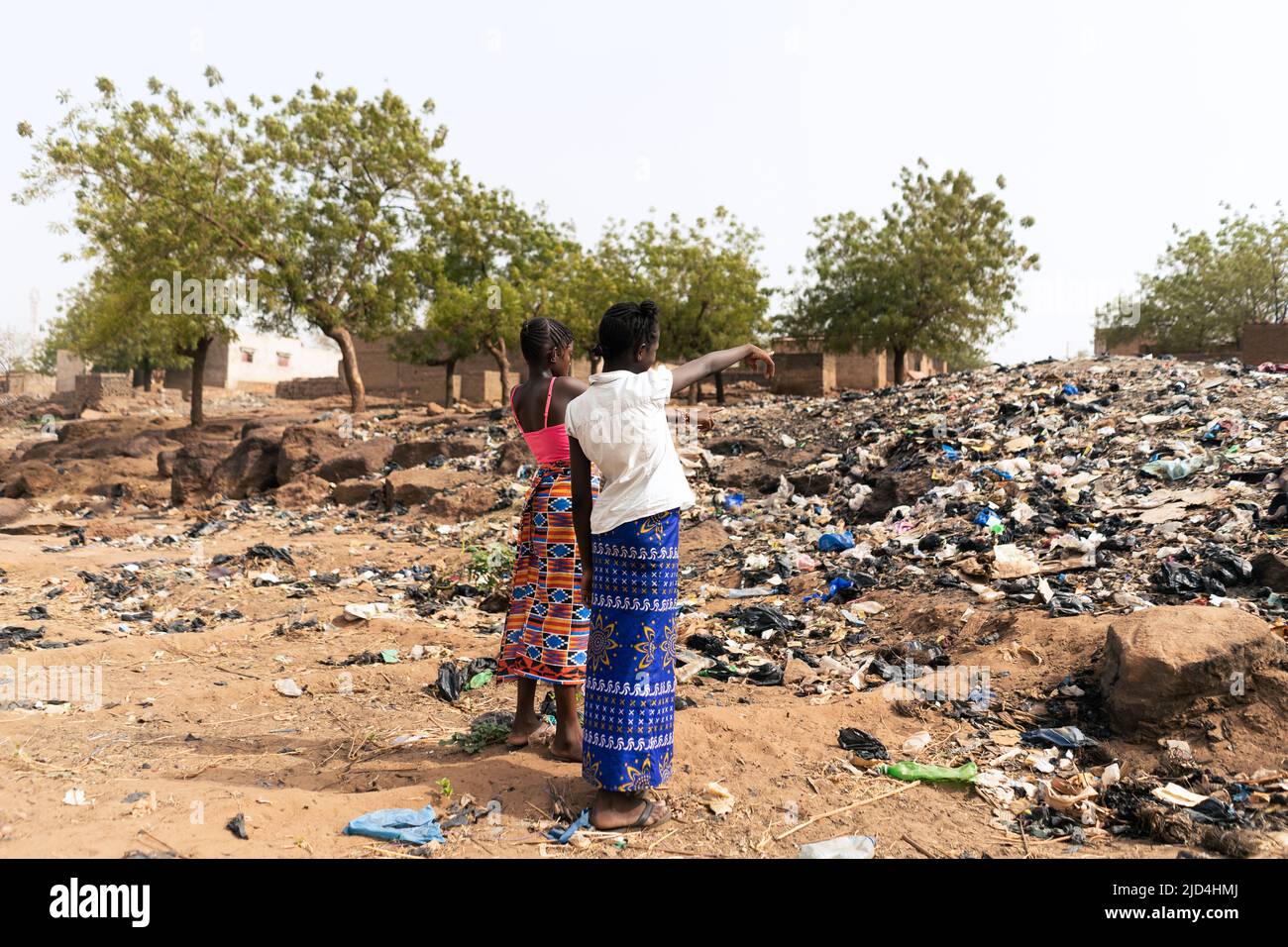 Dos niñas africanas que señalan a la montaña de basura que ocupa la calle de su aldea indicando la mala gestión de los desechos que afligen Foto de stock