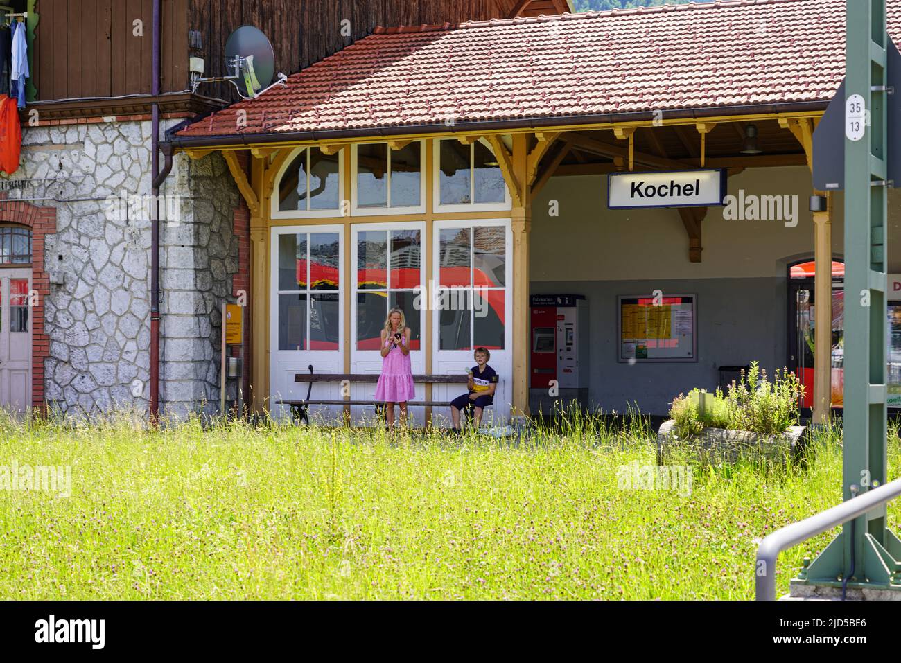Una mujer y un niño esperan en la zona de espera exterior de la estación de tren bávara en Kochel, Baviera, Alemania, 18.6.22 Foto de stock