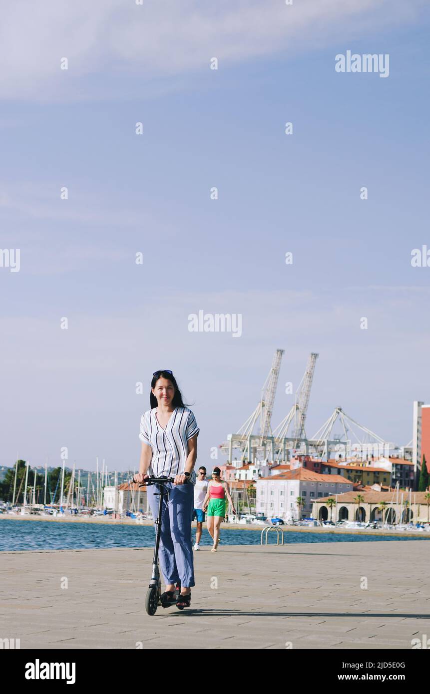 Joven hermosa estudiante asiática, con una mochila, camina en el parque con  un scooter eléctrico, en el verano en la calle Fotografía de stock - Alamy