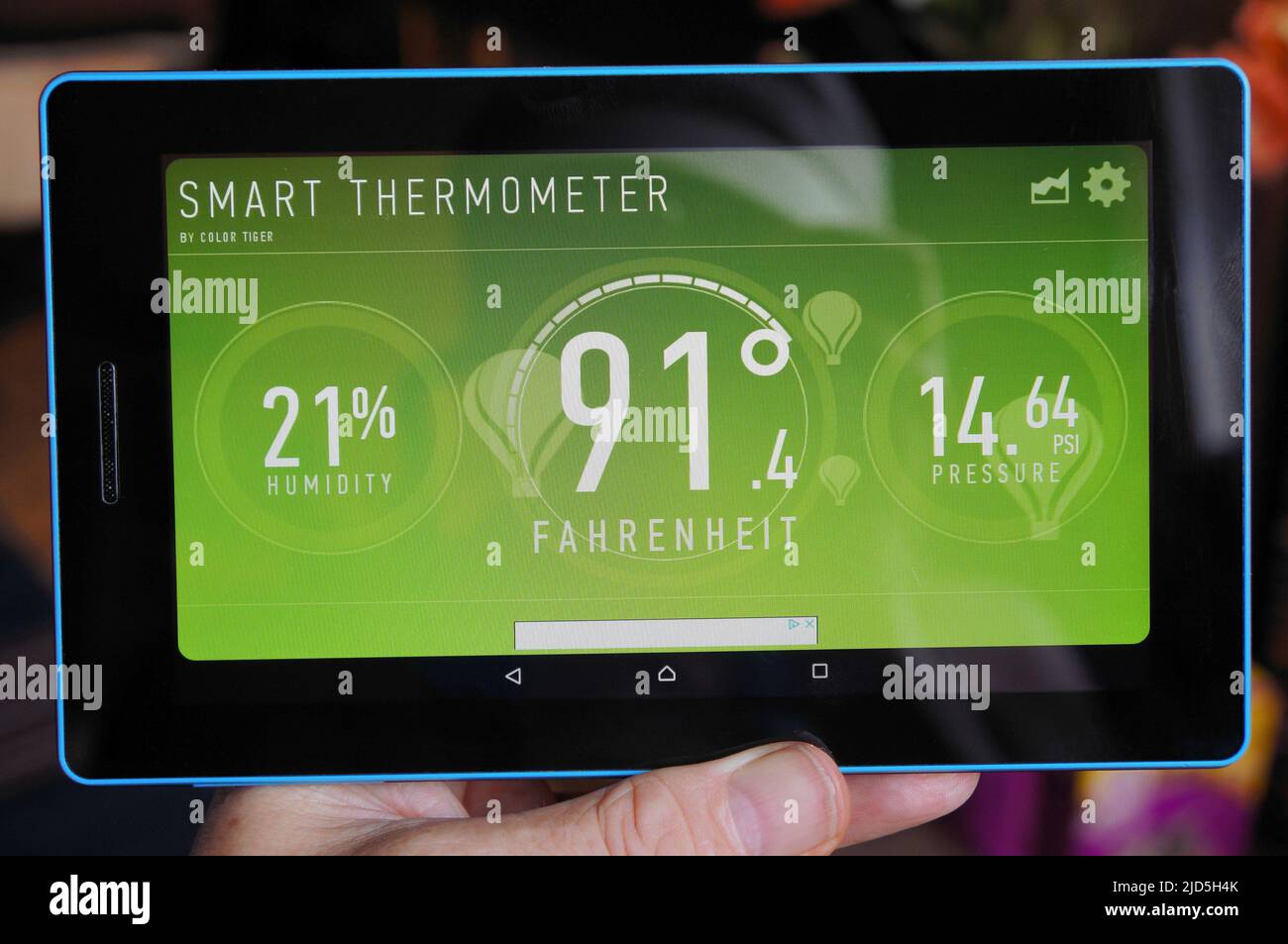 Con la mano sujetando un tablet PC que muestre la temperatura y la humedad actuales en la aplicación meteorológica. Foto de stock
