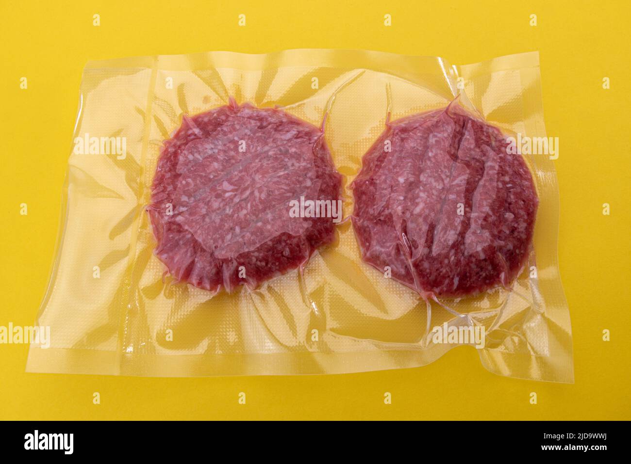 Hamburguesa de carne para hamburguesa en envasado al vacío sellado para cocinar al vacío aislado sobre fondo amarillo Foto de stock