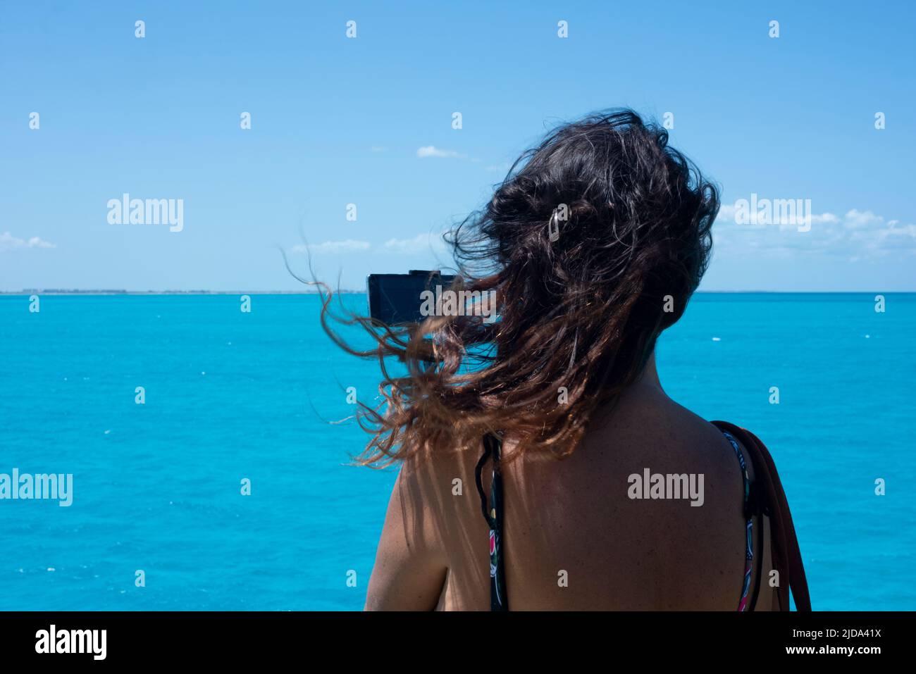 Mujer fotografiando el mar Caribe contra el cielo azul desde la cubierta de un barco Foto de stock