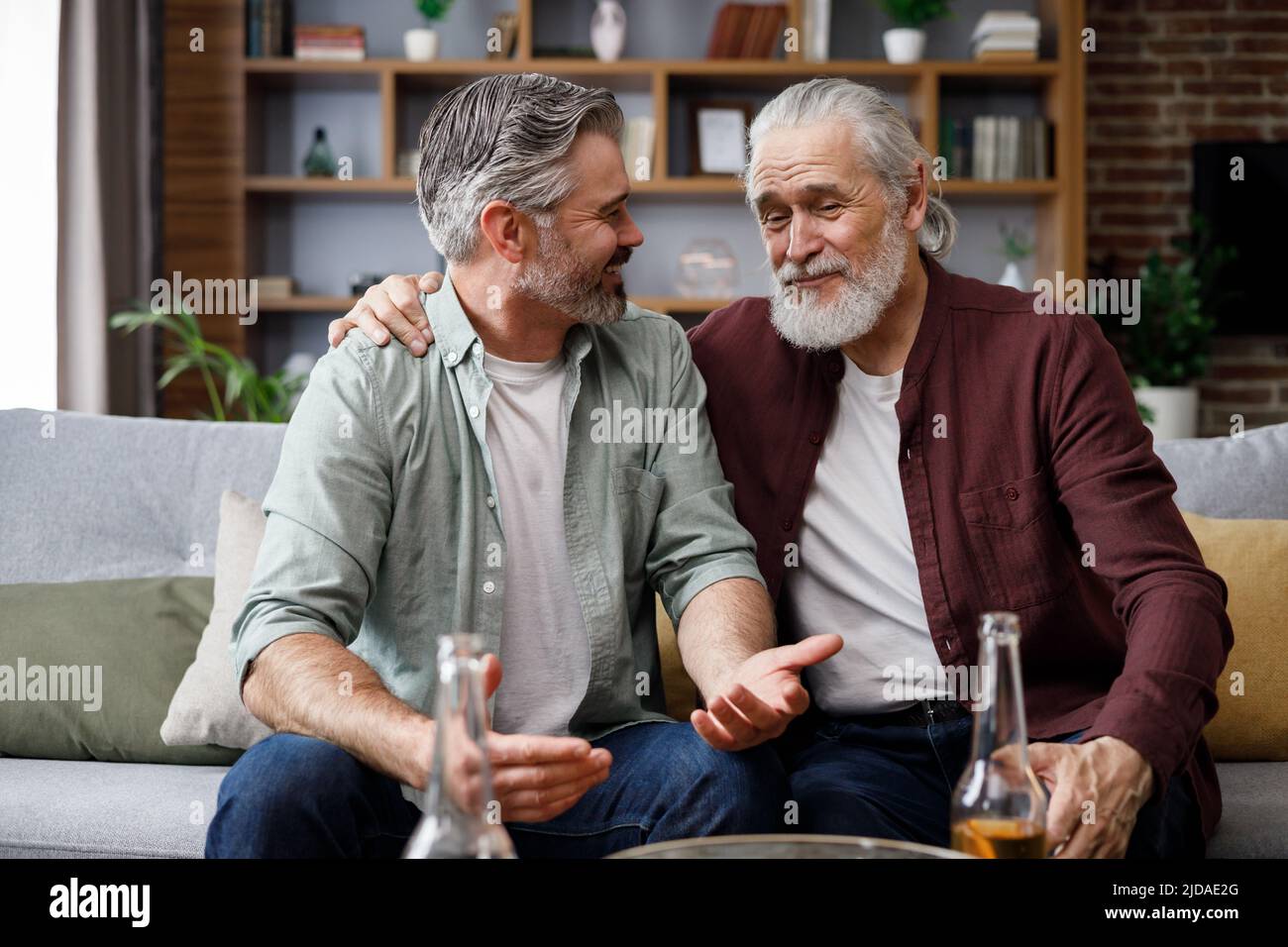 Día de los padres. Hijo adulto con padre mayor bebiendo cerveza sentado en  el sofá de la casa. Dos generaciones de familia disfrutan de una  conversación agradable, hablar, compartir Fotografía de stock -