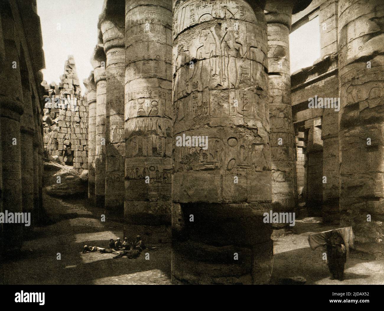 Esta imagen de 1910 muestra las ruinas de la Sala de Columnas de Karnak. El Gran Salón Hipoestilo Karnak está compuesto de 134 columnas gigantes de arenisca en forma de tallos de papiro. Doce grandes columnas en su nave central tienen más de 70 pies de altura y están cubiertas por enormes capiteles abiertos de flores de papiro. El eje principal este-oeste de la sala hipostyle está dominado por una doble fila de 12 columnas gigantes. Esta imagen es de un fotograbado en Egipto por los arqueólogos alemanes Ebers y Junghaendel. Foto de stock