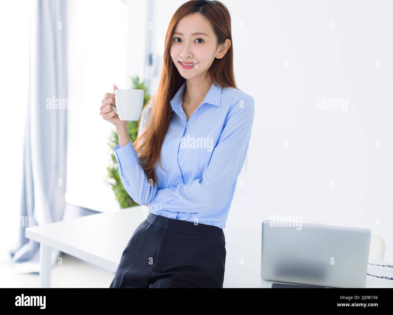 Joven mujer de negocios sonriendo y sosteniendo una taza de café trabajando en la oficina. Foto de stock
