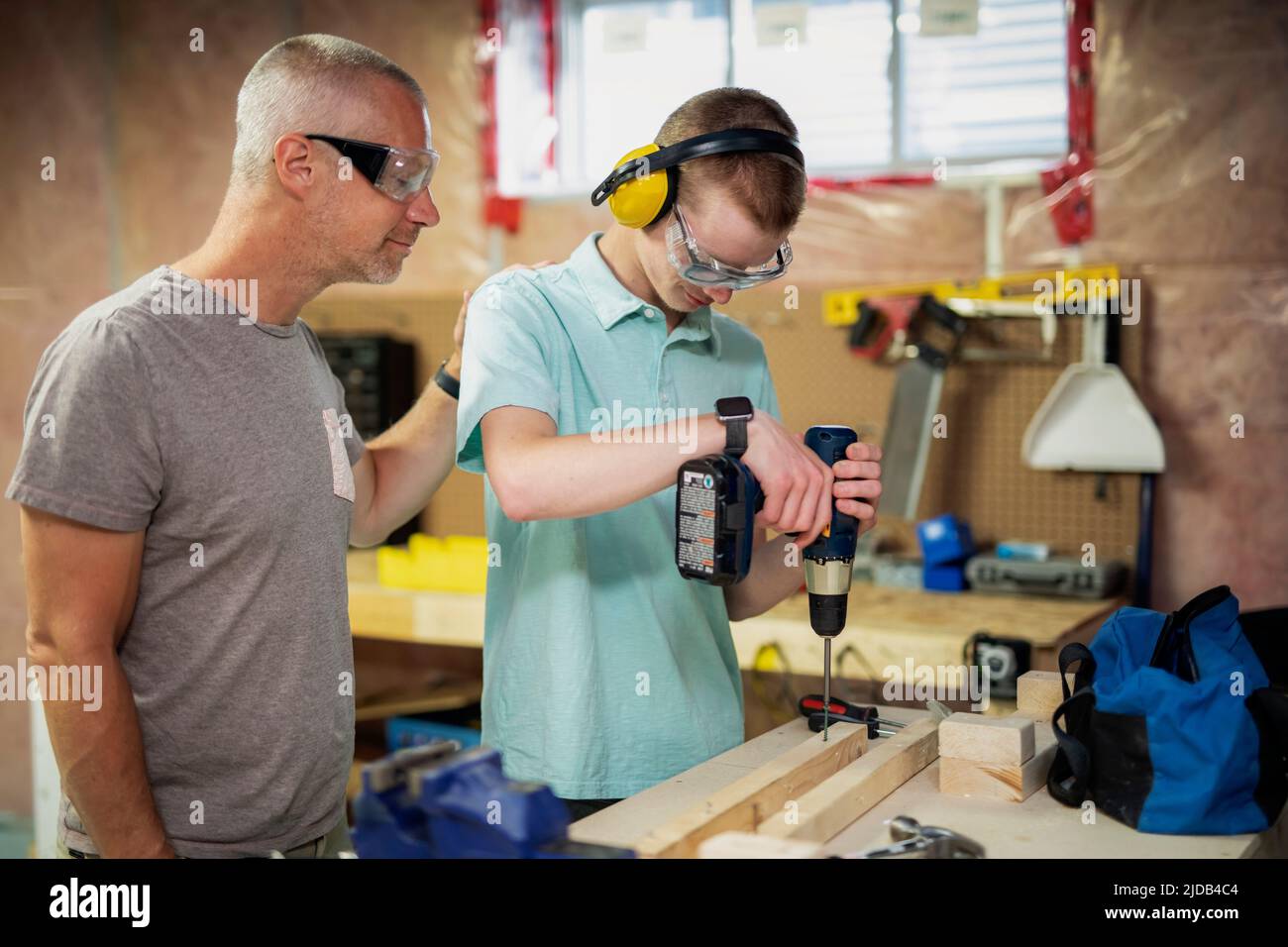 Joven haciendo carpintería en su sótano mientras su padre mira; Edmonton, Alberta, Canadá Foto de stock